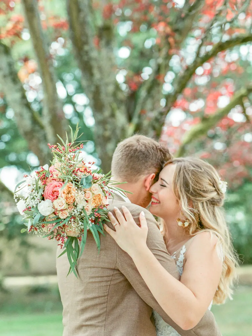 Couple embracing with a peach and coral bouquet, Domaine de Larchey