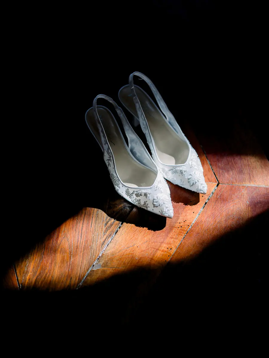 Escarpins de mariée en dentelle posés dans un rai de lumière sur un parquet sombre