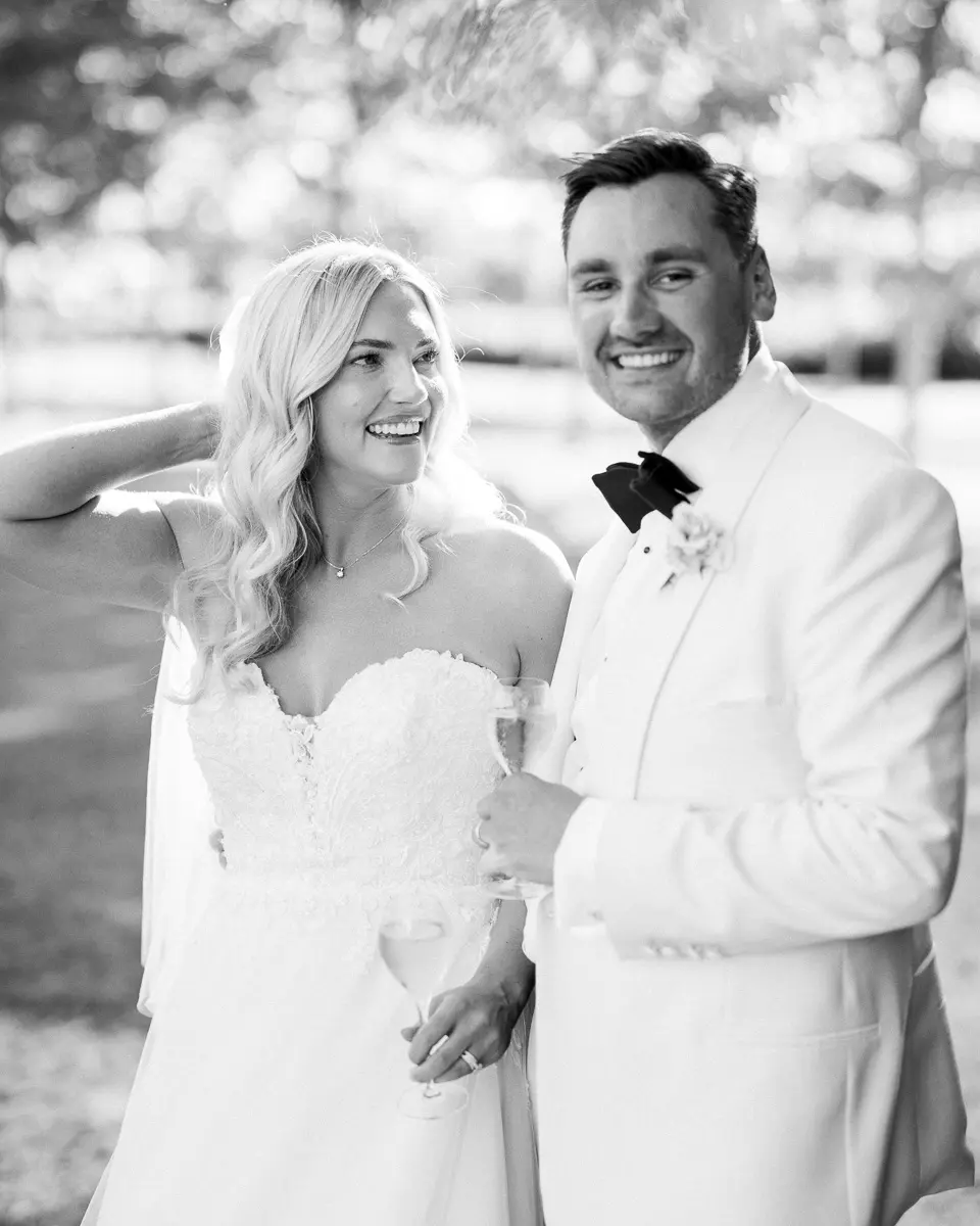 Alice and Charles smiling in black and white, the groom in a white tuxedo
