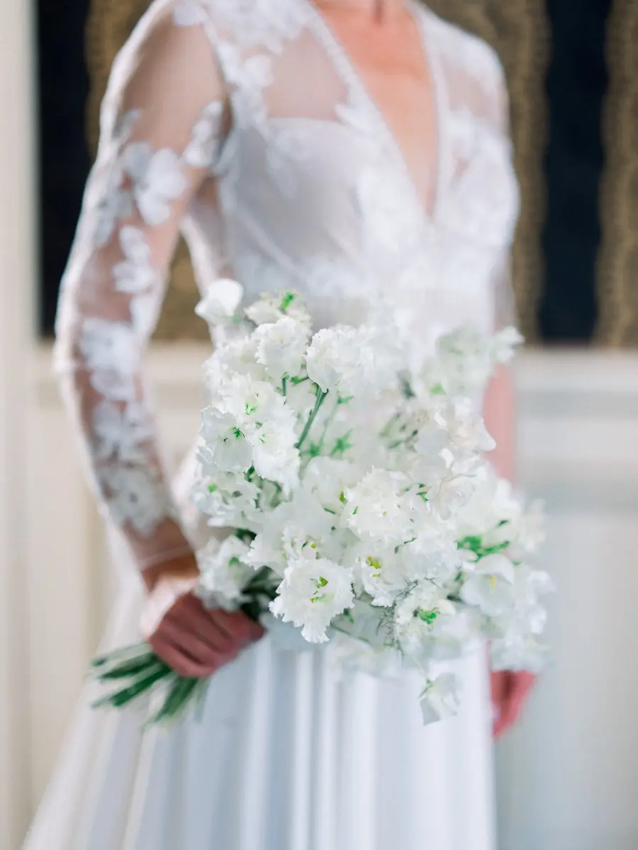 Mariée en robe à manches de dentelle tenant un bouquet de fleurs blanches