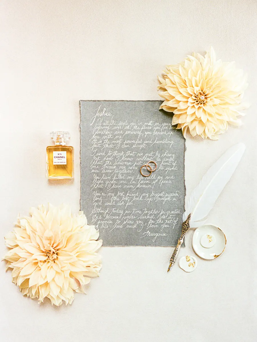 Lettre manuscrite, alliances, parfum et plume posés à plat avec des dahlias