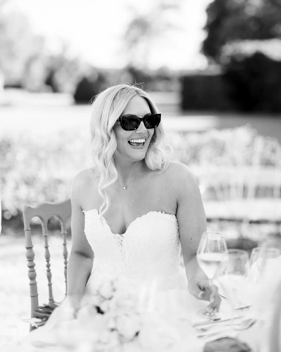 Mariée en lunettes de soleil riant à table, en noir et blanc