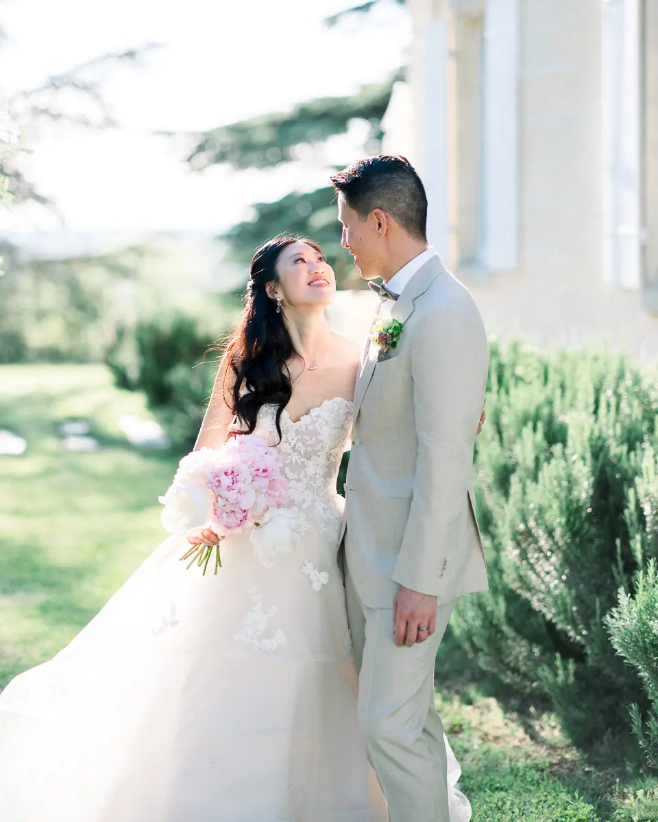 Mariés souriants avec un bouquet rose dans le parc du Château Gassies