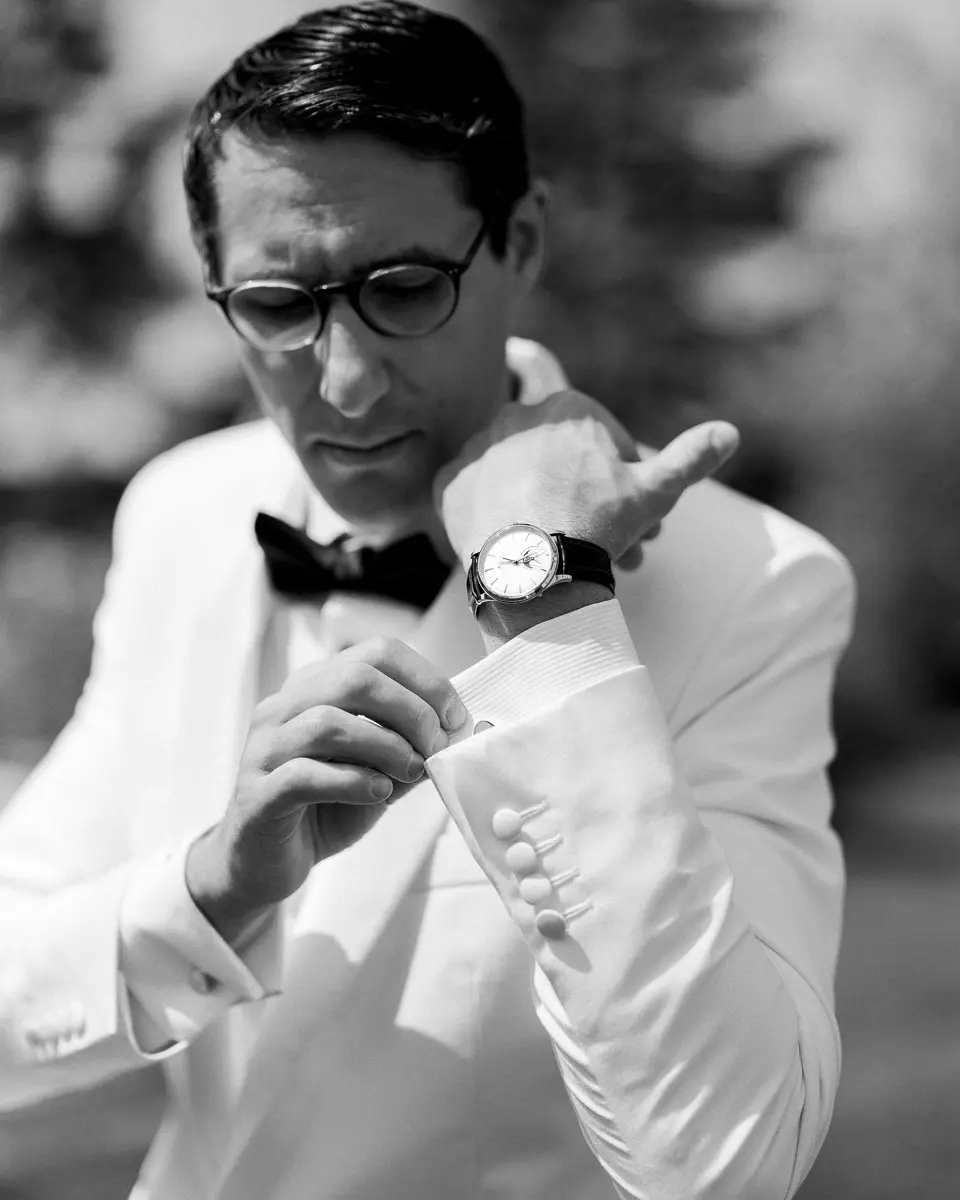 Marié en smoking blanc ajustant sa manchette, en noir et blanc