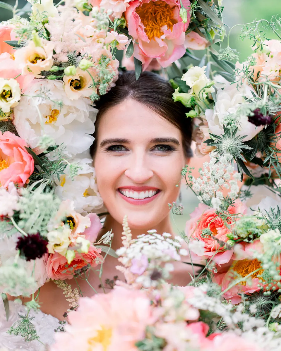 Portrait d'une mariée souriante entourée de fleurs roses et corail