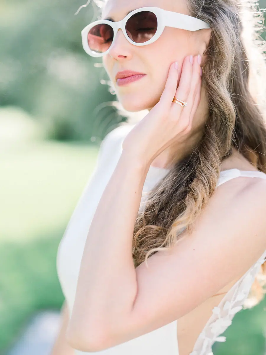 Mariée en lunettes de soleil blanches, la main sur la joue, en lumière naturelle à Bordeaux