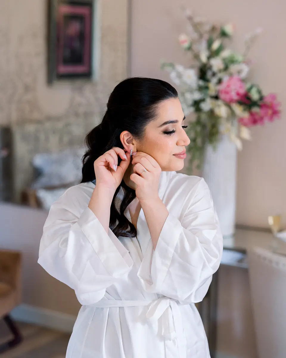 Mariée en peignoir de soie ajustant ses boucles d'oreilles le matin du mariage