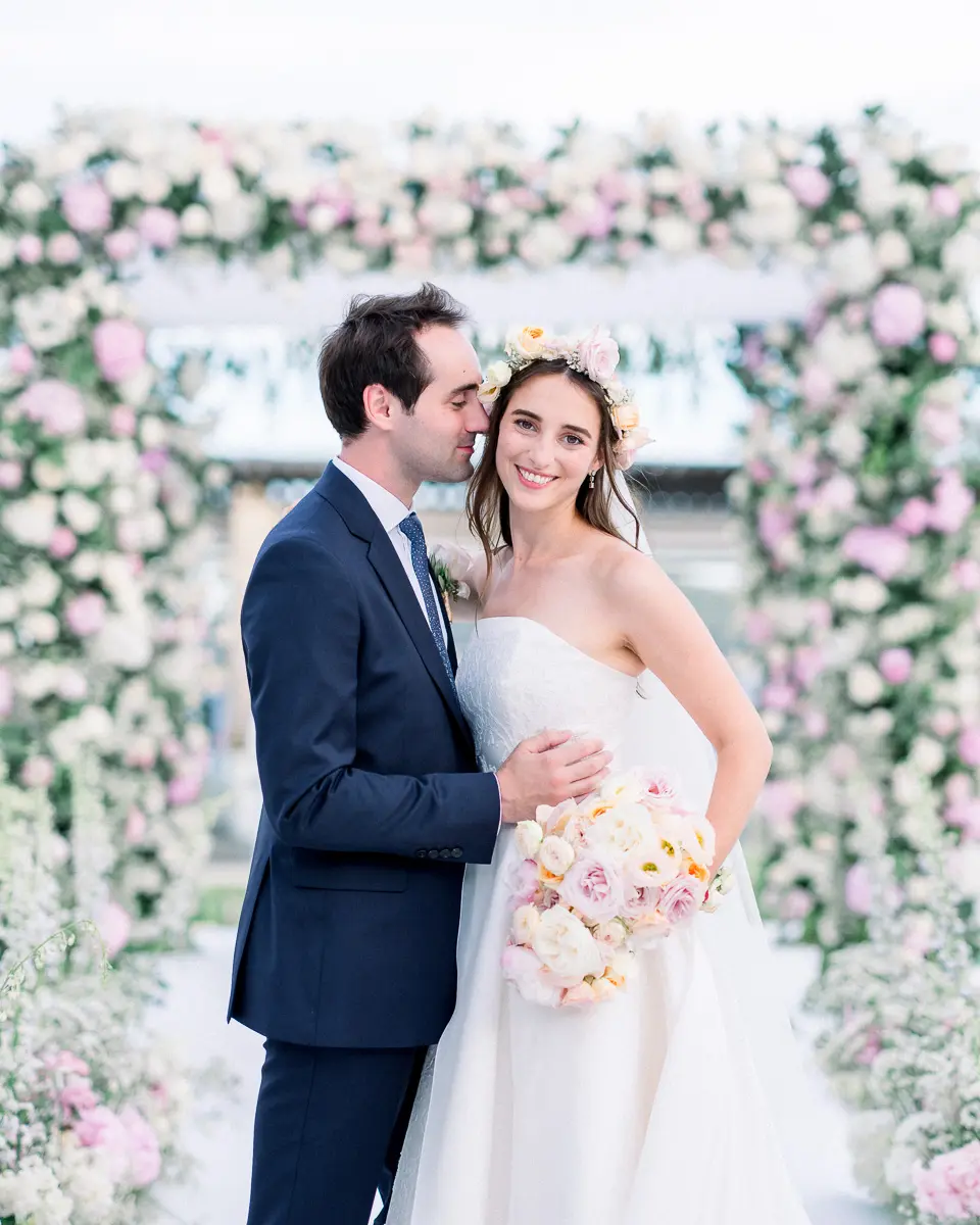 Bride and groom beneath a pink floral arch in Beauvallon, facing Saint-Tropez