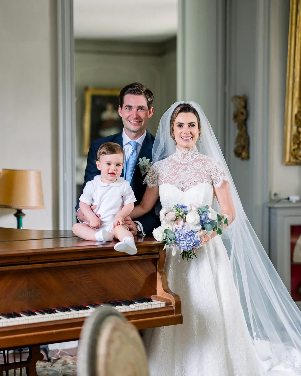 Mariés et leur bébé posant près d'un piano dans le salon d'un château